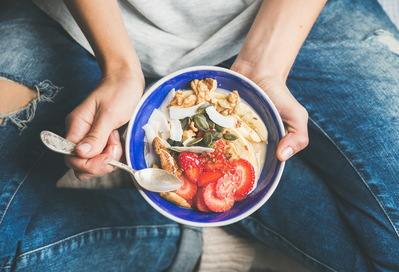 person holding bowl of yogurt with granola and berries